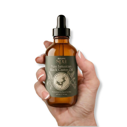 Hand holding a bottle of Pure Jamaican Black Castor Oil with a visible label | Omiana Spa